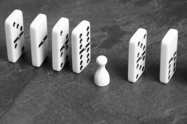 A white wooden pawn stands between lined up dominoes and prevents the vicious circle or the chain reaction from continuing - concept with dominoes and playing figures as creative support  clipart