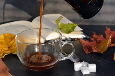 Bir cam fincan içine bir sonbahar ayarı kahve dökün-bir cam fincan kuru ve renkli sonbahar yaprakları ve arka planda bir kitap yanında standig ve birisi içine kahve dökme olduğunu