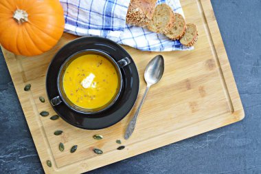 Küçük bir kapta kabak krema çorbası ve yanında bütün bir kabak ve dilimlenmiş ekmek ile mutfak yüzeyinde ahşap bir tahta üzerinde - sonbahar şölen 