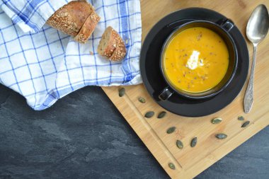 Küçük bir kapta kabak krema çorbası ve yanında bütün bir kabak ve dilimlenmiş ekmek ile mutfak yüzeyinde ahşap bir tahta üzerinde - sonbahar şölen 