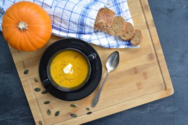 Küçük bir kapta kabak krema çorbası ve yanında bütün bir kabak ve dilimlenmiş ekmek ile mutfak yüzeyinde ahşap bir tahta üzerinde - sonbahar şölen 