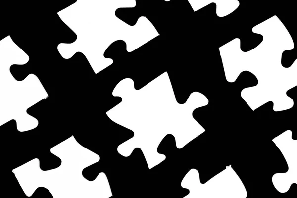 White puzzle pieces against a black background with a certain distance between the individual parts - concept for sub-steps or sub-elements of a large whole presented with puzzle pieces