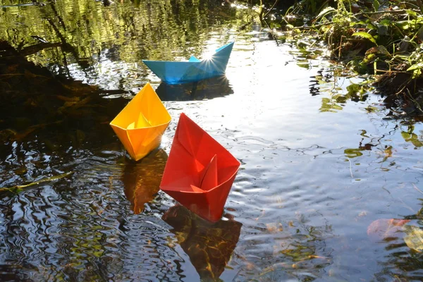 Different colored paper ships swim in a small brook on the surface of which reflects the late autumn sun - Slightly blurred paper ships in bright colors on a lake in late autumn