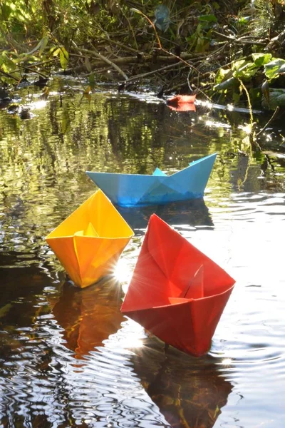 Different colored paper ships swim in a small brook on the surface of which reflects the late autumn sun - Slightly blurred paper ships in bright colors on a lake in late autumn