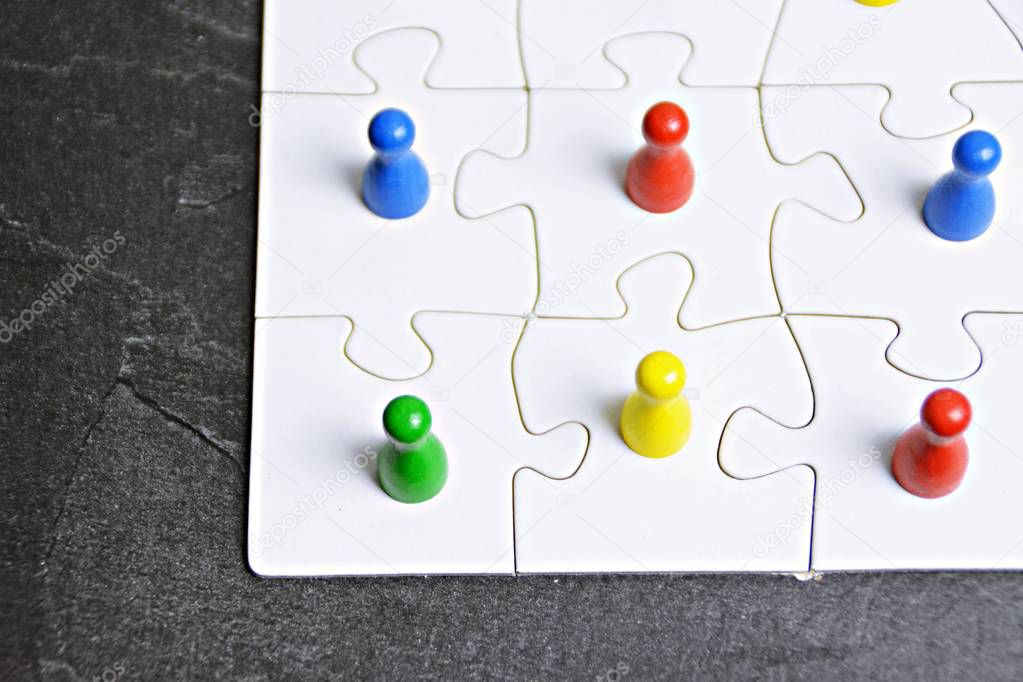 Wooden figures in different colors stand on a puzzle piece each and symbolize that a great project is only possible and feasible with many different characters working together