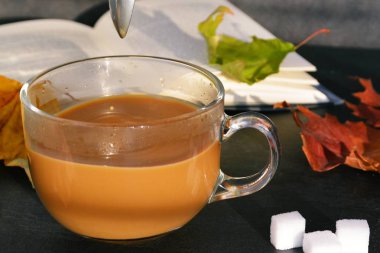 Bir cam fincan içine bir sonbahar ayarı kahve dökün-bir cam fincan kuru ve renkli sonbahar yaprakları ve arka planda bir kitap yanında standig ve birisi içine kahve dökme olduğunu