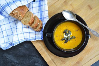 Küçük bir kapta kabak krema çorbası ve yanında bütün bir kabak ve dilimlenmiş ekmek ile mutfak yüzeyinde ahşap bir tahta üzerinde - sonbahar şölen 