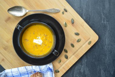 Küçük bir kapta kabak krema çorbası ve yanında bütün bir kabak ve dilimlenmiş ekmek ile mutfak yüzeyinde ahşap bir tahta üzerinde - sonbahar şölen 