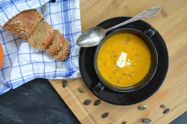 Küçük bir kapta kabak krema çorbası ve yanında bütün bir kabak ve dilimlenmiş ekmek ile mutfak yüzeyinde ahşap bir tahta üzerinde - sonbahar şölen 