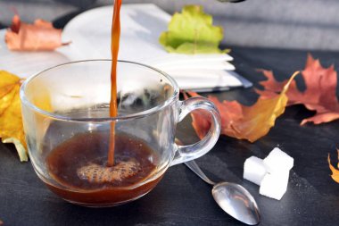 Bir cam fincan içine bir sonbahar ayarı kahve dökün-bir cam fincan kuru ve renkli sonbahar yaprakları ve arka planda bir kitap yanında standig ve birisi içine kahve dökme olduğunu