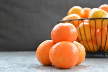 Dört mandalina yığını arka planda mandalina bir sepet ve koyu gri arka plan ile bir mermer plaka üzerinde oturur