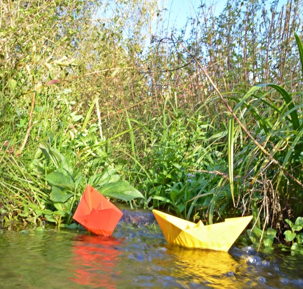 Different colored paper ships swim in a small brook on the surface of which reflects the late autumn sun - Slightly blurred paper ships in bright colors on a lake in late autumn