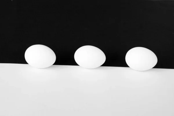 白いカップを持つ鶏の卵は 半分の白と半分の黒の背景の前に横たわっている 白い卵と少し影の背景として強いコントラストを持つコンセプト — ストック写真