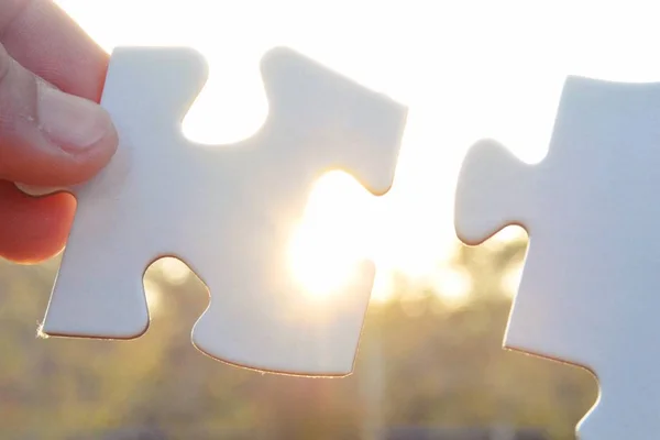 closeup view of hands holding big puzzle pieces in front of sunlight