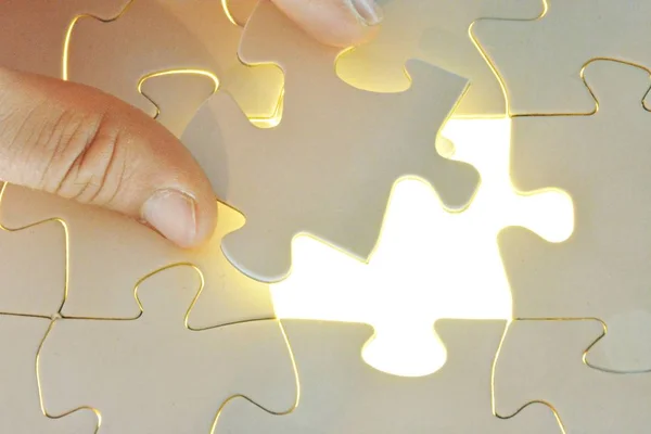 Yakın çekim bir el Toplam bulmaca beyaz bir puzzle parçası koyarak. Eksik parçanın yüzeyi parlak parlar-tamamlanmış bir projenin radyant başarısının sunumu için konsept 
