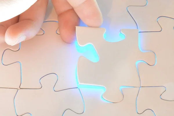 Close-up of a hand putting a white puzzle piece in a total puzzle. The surface of the missing part shines brightly - Concept for the presentation of the radiant success of a completed project