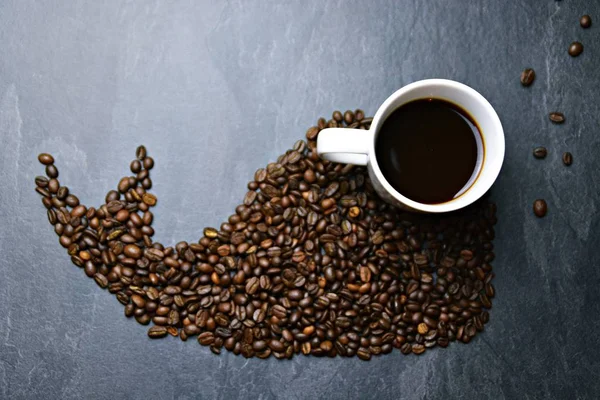 Coffee beans on a black background form the silhouette of a whale and two cups of coffee form their eyes - concept with coffee and whale