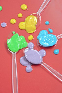 Düz bir arka planda boya farklı damla ile şeffaf kaşıklar-metin alanı ile arka plan olarak renk ile plastik kaşık 