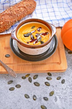 Küçük bir kapta kabak krema çorbası ve yanında bütün bir kabak ve dilimlenmiş ekmek ile mutfak yüzeyinde ahşap bir tahta üzerinde - sonbahar şölen 