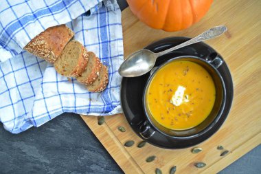 Küçük bir kapta kabak krema çorbası ve yanında bütün bir kabak ve dilimlenmiş ekmek ile mutfak yüzeyinde ahşap bir tahta üzerinde - sonbahar şölen 