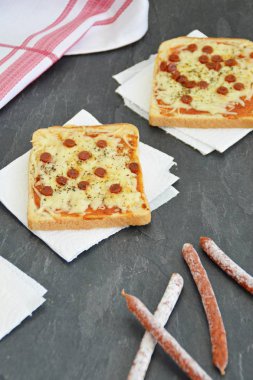 Yanında kırmızı çay havlusu ile mutfak yüzeyinde domates soslu ev yapımı tost, salam dilimleri ve peynir