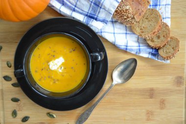 Küçük bir kapta kabak krema çorbası ve yanında bütün bir kabak ve dilimlenmiş ekmek ile mutfak yüzeyinde ahşap bir tahta üzerinde - sonbahar şölen 