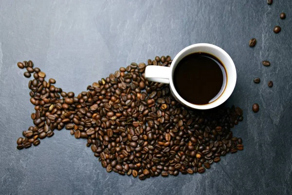 Coffee beans on a black background form the silhouette of a whale and two cups of coffee form their eyes - concept with coffee and whale