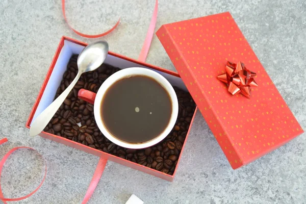 A cup full of coffee is in a Christmas gift box with coffee beans in it - coffee as a treat and gift for Christmas nicely packaged