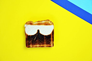 Renkli bir yüzeyde tost yatıyor. Tost her yerde aynı tost değil, ama güneş gözlüğü şeklinde tadı olmayan noktalar var-yaz aylarında güneş yanığı için soyut konsept 