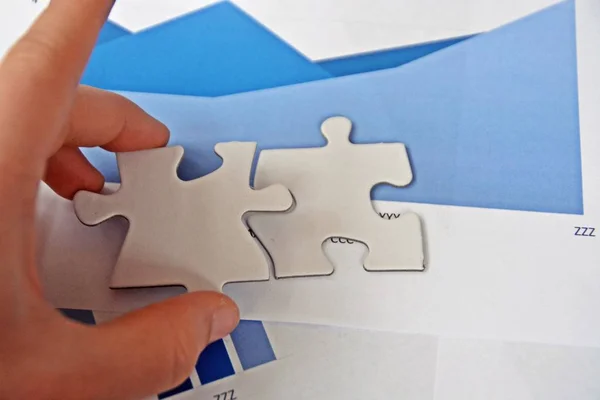 A young man holds a piece of the puzzle in his hand and behind it all sorts of statistics - a close-up on the hand - concept with puzzle pieces and statistics on strategy design