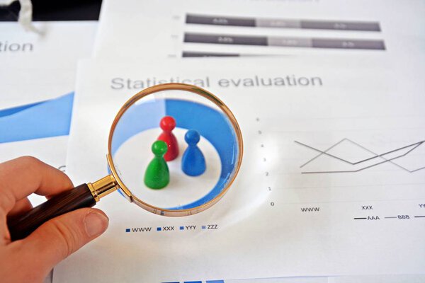 A young man is holding a magnifying glass in his hand, looking at statistic figures - a business concept on the subject of sampling and selecting the right target group and examining it 