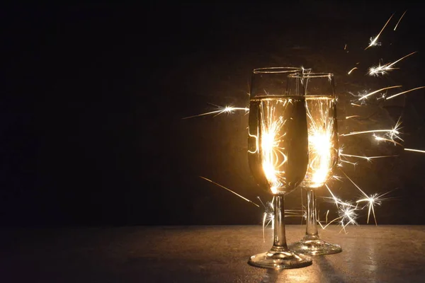 两个充满香槟的长笛站在黑暗中的火花 照亮他们与火花从后面 概念的新年前夜和烟花的空间文本和其他对象 — 图库照片