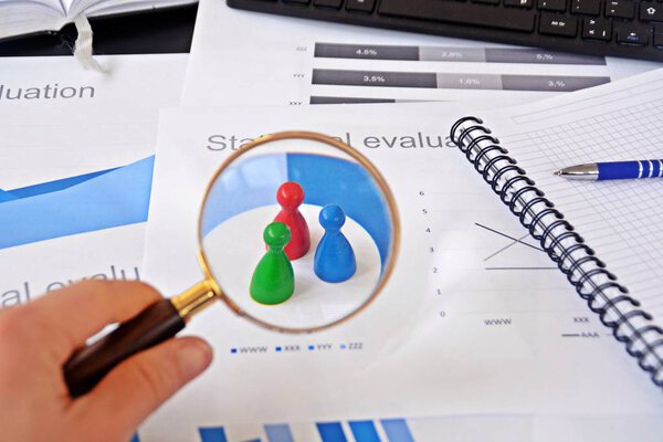 Молодой человек держит увеличительное стекло в руке, рассматривая статистические данные - бизнес-концепцию на тему отбора проб и выбора правильной целевой группы и изучения ее
 