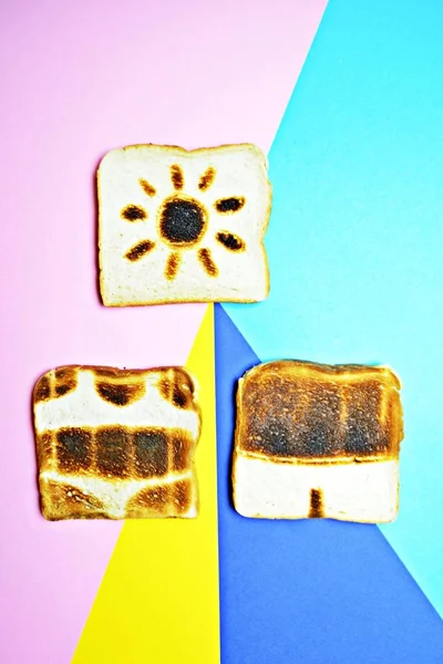 Three toasts lie on a colorful background - these are not toasted on the whole surface but show the contours of trunks and bikini and those of a sun - concept of sunburn presented with toasts