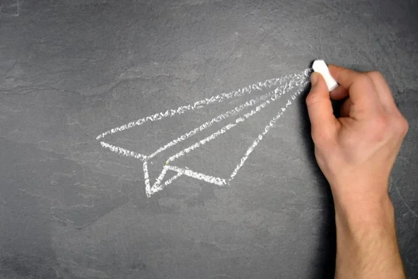 With a chalk drawn a paper plane and a dashed way on a dark marble surface - background with a flying paper plane