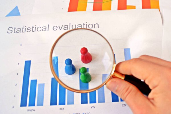 A young man is holding a magnifying glass in his hand, looking at statistic figures - a business concept on the subject of sampling and selecting the right target group and examining it 
