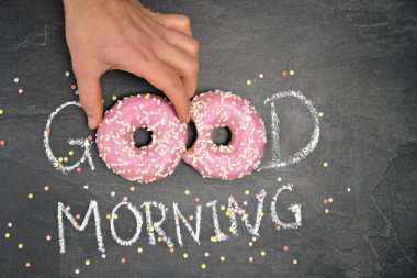 Tebeşir karanlık bir taş yüzeye yazıldı. Günaydın, O kelimeden O kelime beyaz Sprinkles ile iki pembe donut ile değiştirildi-tatlı donut ile güne mutlu başlangıç