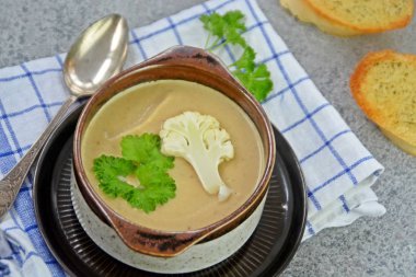 Taze yapılmış ev yapımı karnabahar çorbası maydanoz ve tost beyaz ekmek ile ot tereyağı yayılmış bir mutfak yüzeyi-sağlıklı ve vejetaryen öğle yemeği ile karnabahar ve krem