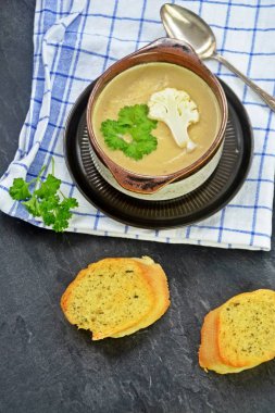 Taze yapılmış ev yapımı karnabahar çorbası maydanoz ve tost beyaz ekmek ile ot tereyağı yayılmış bir mutfak yüzeyi-sağlıklı ve vejetaryen öğle yemeği ile karnabahar ve krem