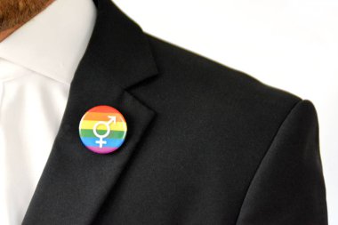 20'li yaşlarının ortasında bir adam takım ceketinde transseksüel sembolü olan bir düğme takıyor - Çalışma Hayatında Kabul ve Hoşgörü Kavramı