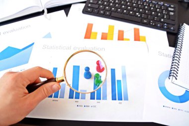 Genç bir adam, istatistik rakamları bakarak, elinde bir büyüteç tutuyor-örnekleme ve doğru hedef grubu seçerek ve onu inceleyerek konu üzerinde bir iş kavramı 