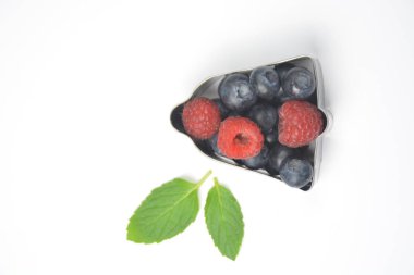 Kurabiye kesici nane ile beyaz bir arka plan önünde yaban mersini ve ahududu ile dolu-çerez formunda taze çilek ile kavramı yanında yaprakları 