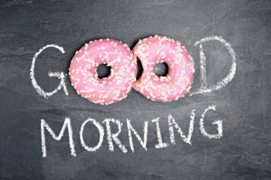 Tebeşir karanlık bir taş yüzeye yazıldı. Günaydın, O kelimeden O kelime beyaz Sprinkles ile iki pembe donut ile değiştirildi-tatlı donut ile güne mutlu başlangıç