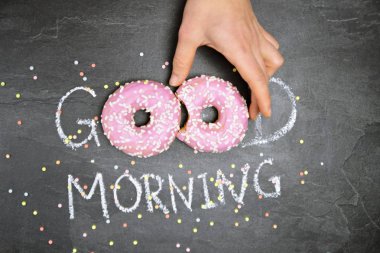 Tebeşir karanlık bir taş yüzeye yazıldı. Günaydın, O kelimeden O kelime beyaz Sprinkles ile iki pembe donut ile değiştirildi-tatlı donut ile güne mutlu başlangıç