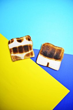 Three toasts lie on a colorful background - these are not toasted on the whole surface but show the contours of trunks and bikini and those of a sun - concept of sunburn presented with toasts  clipart