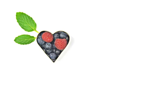 Cookie cutter filled with blueberries and raspberries in front of a white background with mint leaves beside it - concept with fresh berries in cookie form