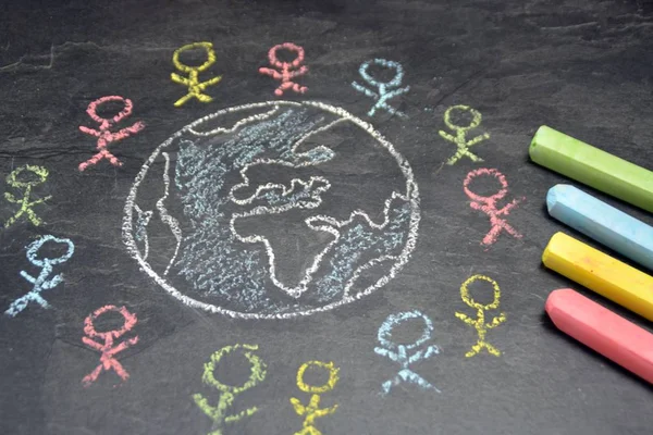 On a dark stone surface, a globe was painted with chalk and different-colored male figures drawn on the outside - concept of diversity and tolerance represented worldwide by a chalk drawing