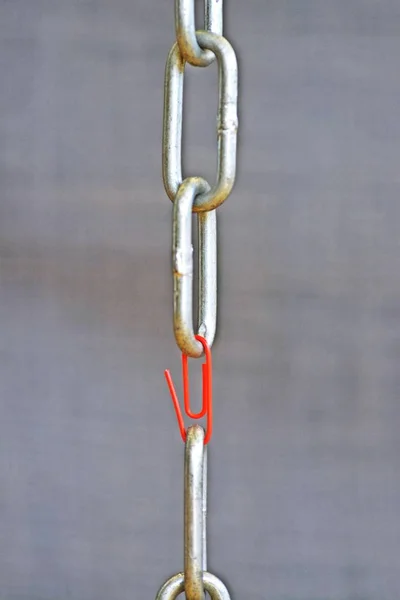 A red paperclip holds two steel chain ends together - Weakest point in chain represented by a paperclip in a normal chain - Concept for teamwork abstract illustrated