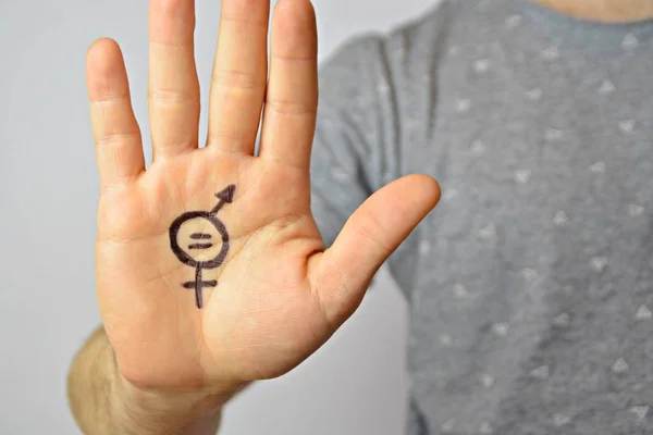 A man in his mid-twenties has painted a sign of gender equality on his hand and shows it to the camera - a concept for demanding equality between men and women