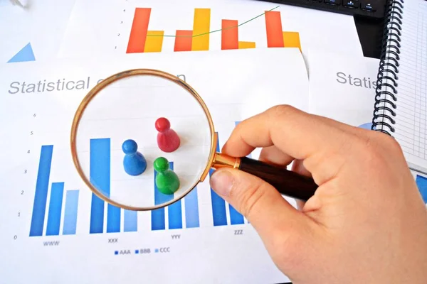 Genç bir adam, istatistik rakamları bakarak, elinde bir büyüteç tutuyor-örnekleme ve doğru hedef grubu seçerek ve onu inceleyerek konu üzerinde bir iş kavramı 